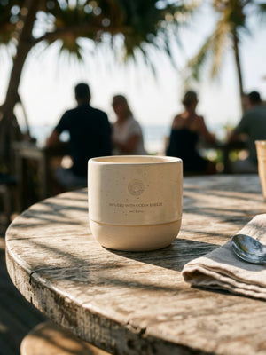 Ocean Mug Cappuccino-Tasse in Sand auf einem Holztisch in einem Strandcafé
