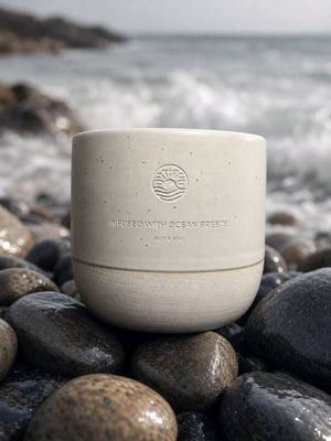 Ocean Mug in sandfarben mit emblem infused with ocean breeze auf Kieselsteinen – jede Tasse ein Unikat