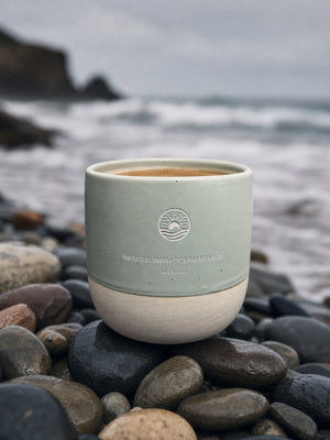 Frisch gebrühter Kaffee im Ocean Mug in Seagrass auf Steinen an der Küste