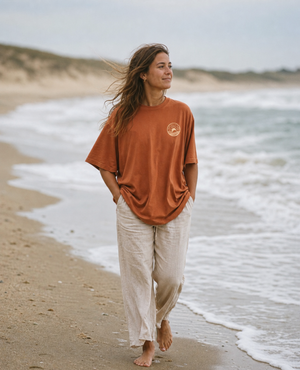 Frau  im oversize SALT Ñ SOUL Beach Shirt mit Sonnenaufgang-Emblem am Strand